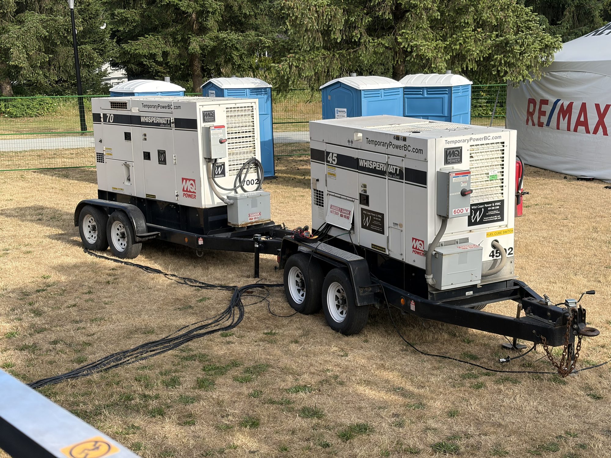 Two WhisperWatt diesel generators on trailers supplying power distribution at a fenced outdoor event site in the Lower Mainland